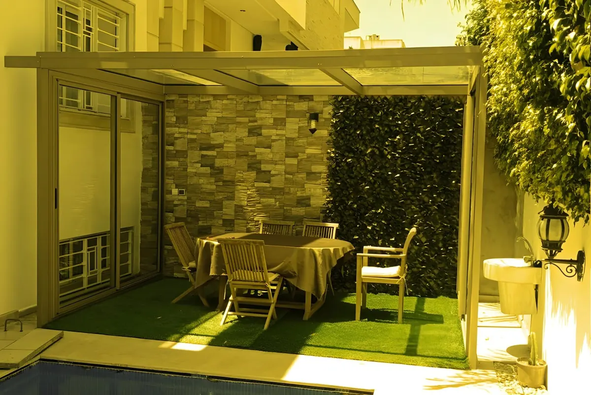 An aluminium pergola over a dining table by a pool.