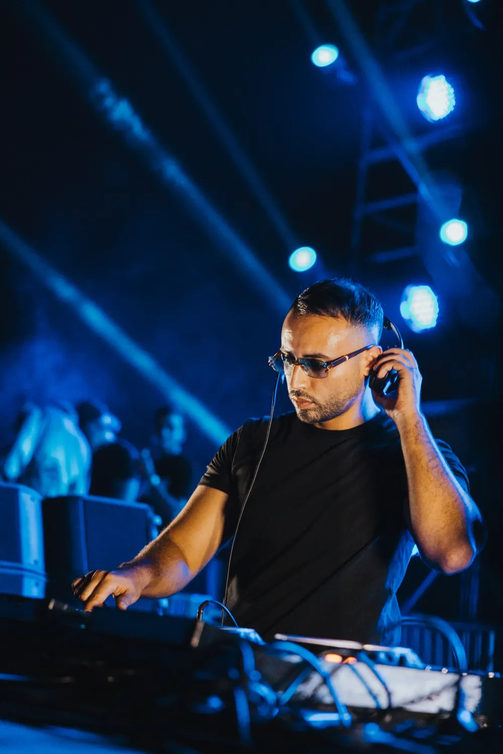 An artist mid-set, headphones on, lit in blue.