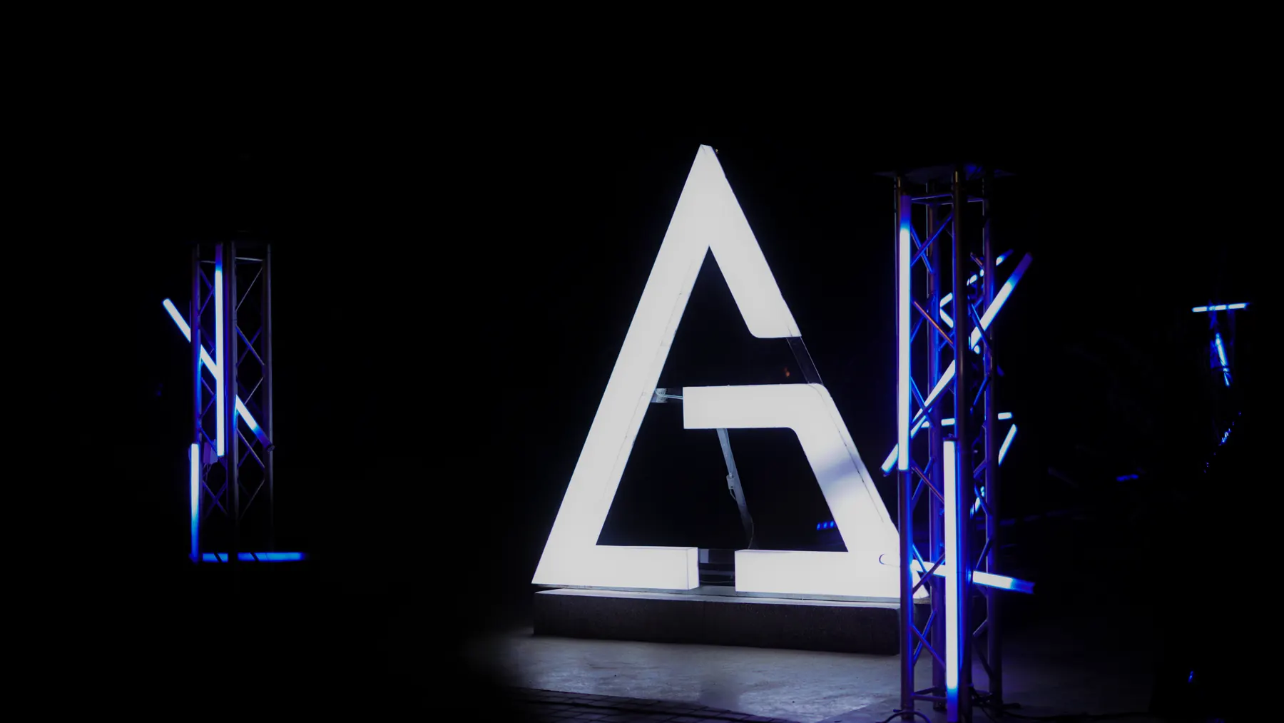 The real triangle installation, lit white between two blue truss towers.